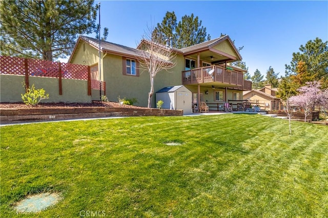 rear view of property with a storage shed, stucco siding, fence, a lawn, and an outdoor structure