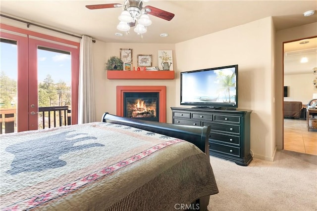 bedroom featuring french doors, light colored carpet, a ceiling fan, a lit fireplace, and access to outside