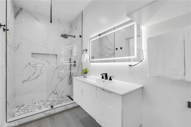 bathroom with a marble finish shower, wood finished floors, and vanity
