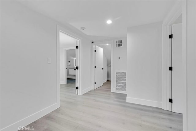 hallway featuring baseboards, light wood finished floors, and visible vents