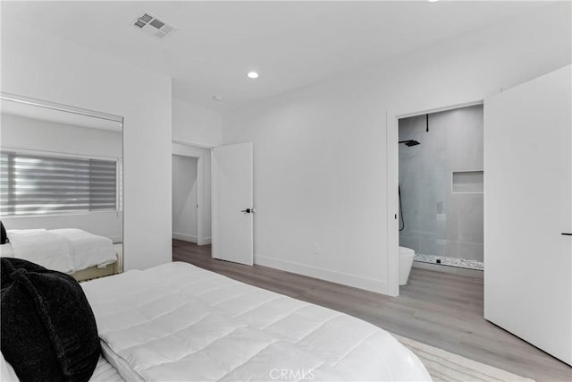 bedroom with ensuite bathroom, wood finished floors, visible vents, recessed lighting, and baseboards