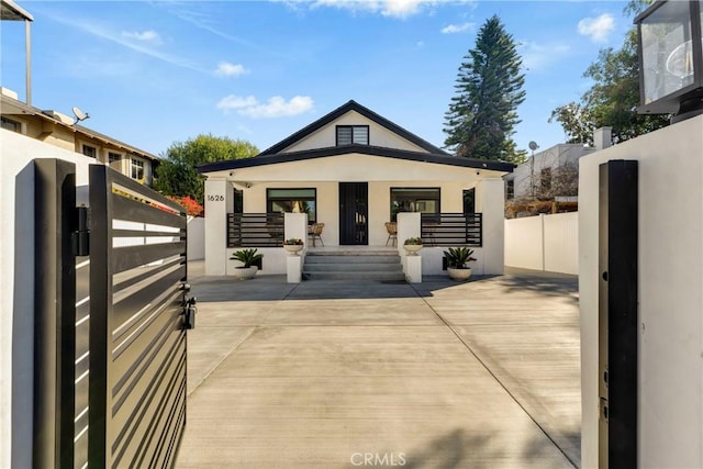 rear view of house with covered porch, stucco siding, a gate, and fence