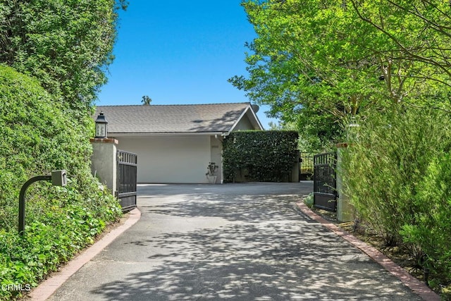 view of side of home with a gate, fence, stucco siding, and driveway