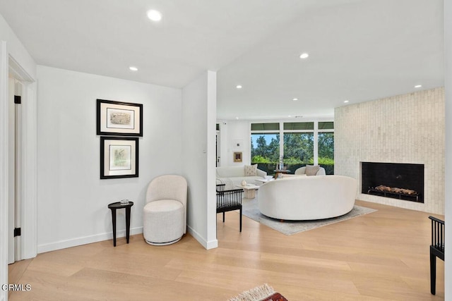 living area with baseboards, recessed lighting, light wood-type flooring, and a large fireplace