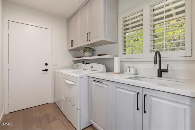clothes washing area with a sink, separate washer and dryer, cabinet space, and light wood-style floors