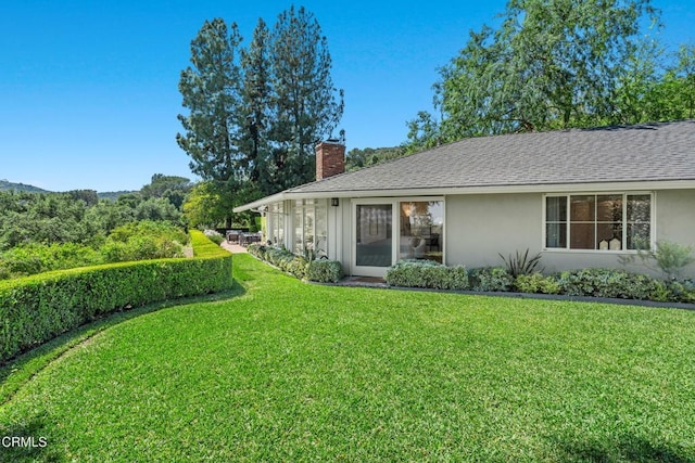 view of side of property with a yard, a shingled roof, stucco siding, and a chimney