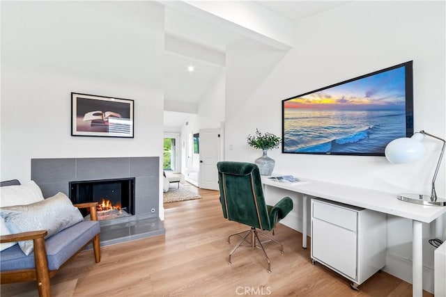 office space featuring light wood-type flooring, a tiled fireplace, and lofted ceiling