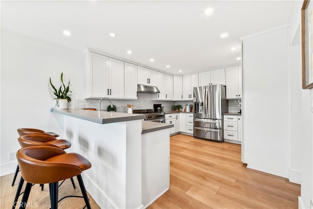 kitchen featuring a peninsula, a breakfast bar, stainless steel appliances, under cabinet range hood, and decorative backsplash