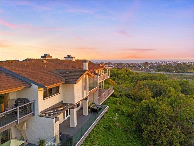 9 Jasmine Creek Dr, Corona Del Mar, CA 92625 - back of house at dusk with stucco siding, a shingled roof, and a balcony
