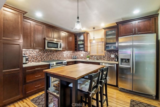 23697 Bowl Rd, Crestline, CA 92325 - kitchen featuring glass insert cabinets, backsplash, light wood-type flooring, decorative light fixtures, and appliances with stainless steel finishes