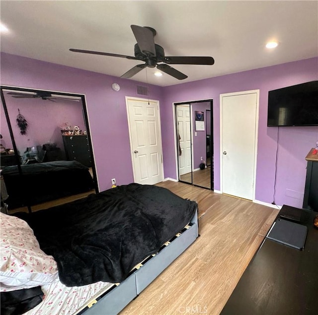 bedroom featuring wood finished floors, a ceiling fan, multiple closets, visible vents, and baseboards