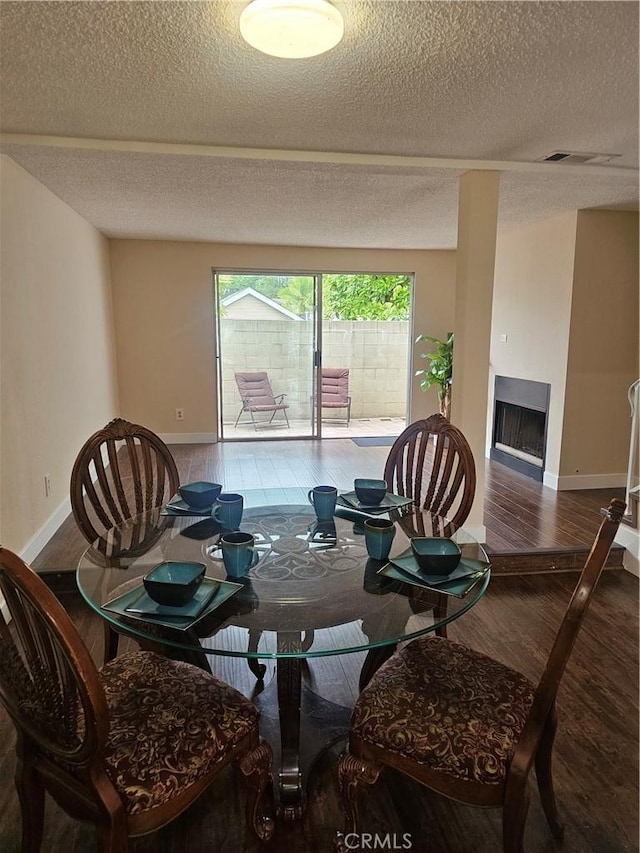 dining room featuring a fireplace, a textured ceiling, baseboards, and wood finished floors