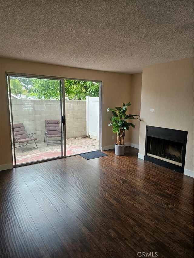 unfurnished living room featuring baseboards, a fireplace, a textured ceiling, and wood finished floors