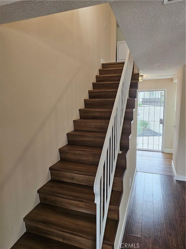 stairs featuring a textured ceiling, wood finished floors, and baseboards