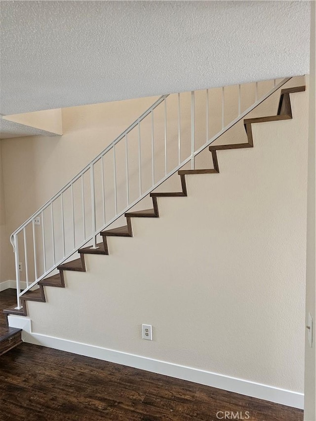 stairway with wood finished floors, baseboards, and a textured ceiling