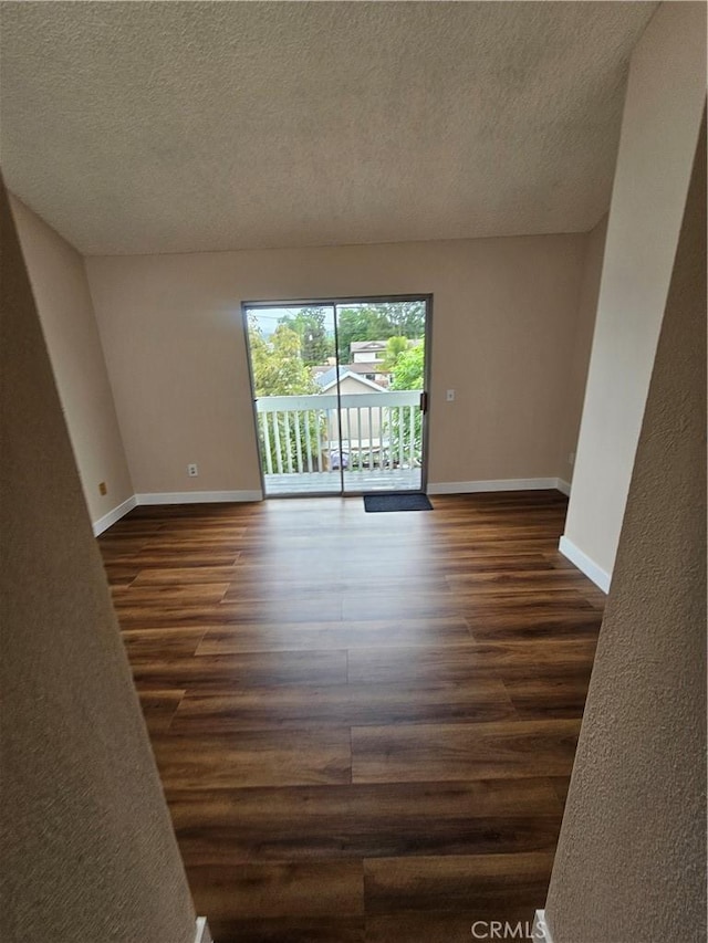 spare room featuring a textured ceiling, dark wood-style flooring, and baseboards