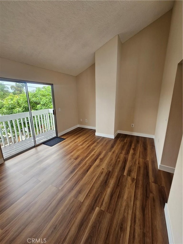 spare room featuring baseboards, dark wood-style flooring, a textured ceiling, and vaulted ceiling