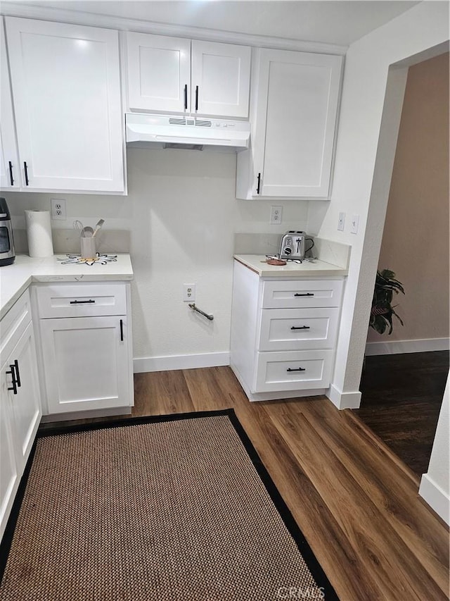 kitchen with white cabinets, dark wood-style flooring, baseboards, under cabinet range hood, and light countertops