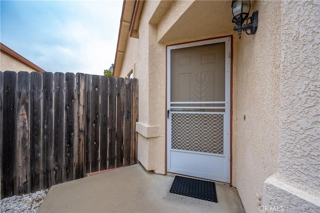 entrance to property featuring stucco siding and fence