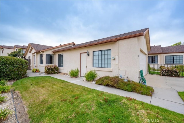 rear view of house featuring a garage, stucco siding, fence, a lawn, and driveway