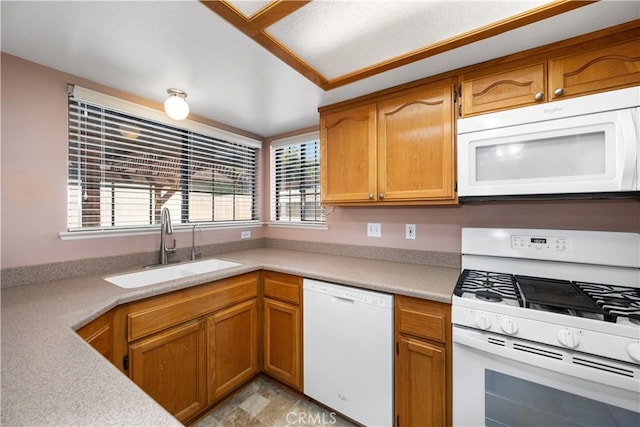 kitchen with brown cabinetry, white appliances, light countertops, and a sink