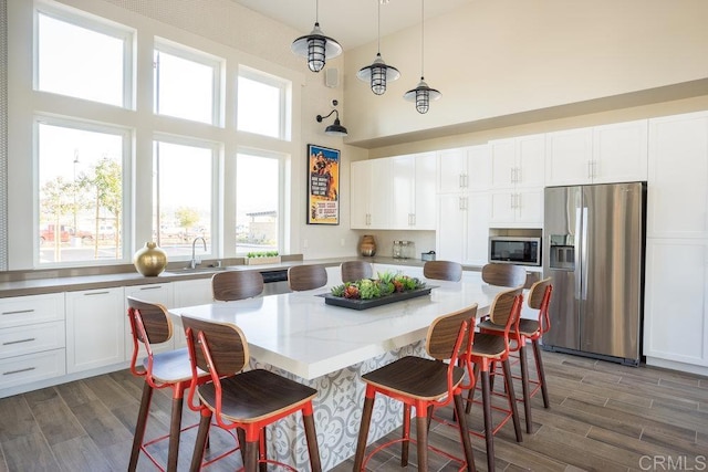 kitchen featuring appliances with stainless steel finishes, a sink, white cabinetry, wood finished floors, and a high ceiling