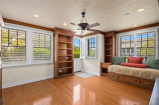 living area featuring ornamental molding, a textured ceiling, light wood-style flooring, a ceiling fan, and baseboards