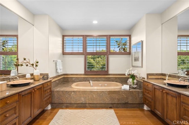bathroom with a garden tub, wood finished floors, two vanities, and a sink