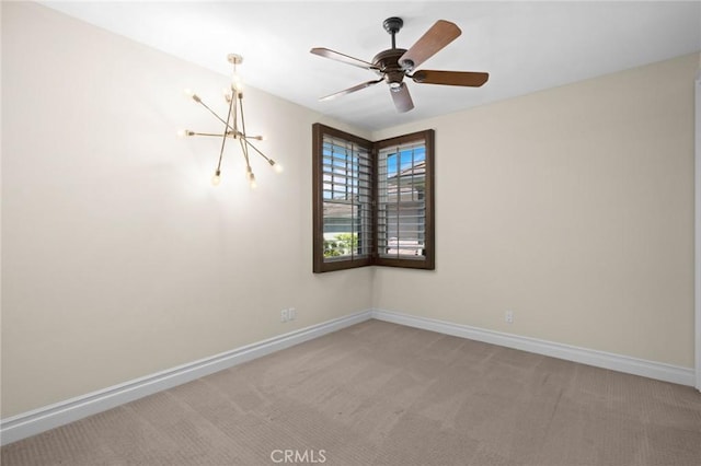 empty room featuring ceiling fan with notable chandelier, carpet floors, and baseboards