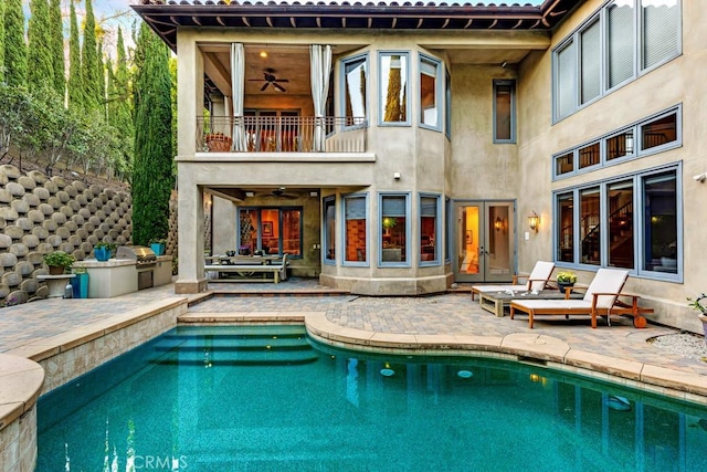 rear view of property featuring a balcony, a ceiling fan, area for grilling, a patio, and stucco siding