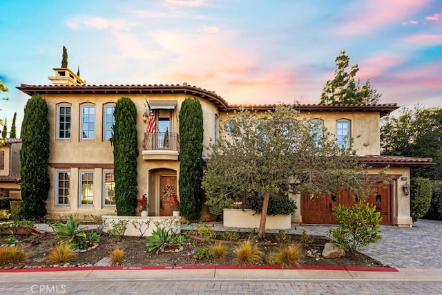 mediterranean / spanish house featuring driveway, a garage, stucco siding, and a balcony
