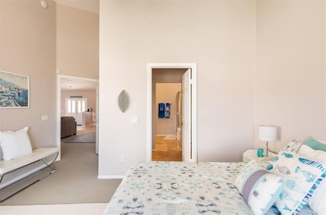 carpeted bedroom with ensuite bath, baseboards, and a towering ceiling