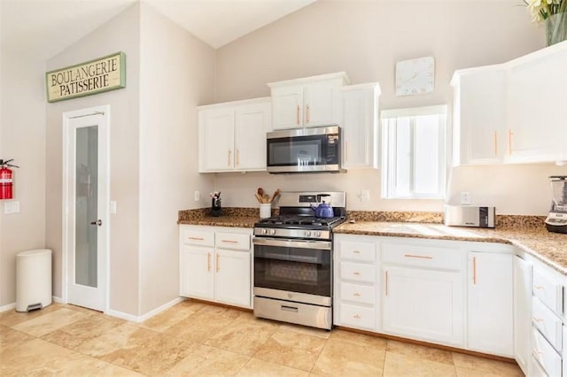 kitchen featuring lofted ceiling, stainless steel appliances, light stone counters, a toaster, and white cabinets