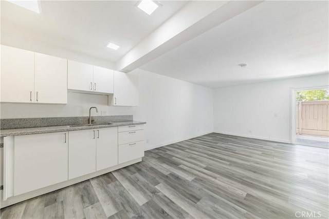 kitchen with baseboards, light stone counters, a sink, light wood-style floors, and white cabinets