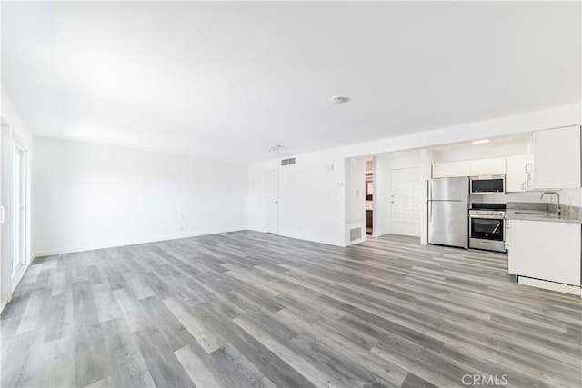 unfurnished living room with baseboards, light wood finished floors, visible vents, and a sink