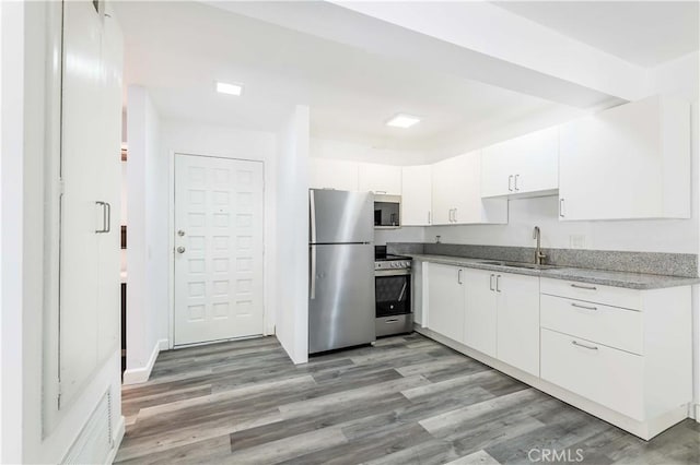 kitchen featuring light stone countertops, light wood finished floors, a sink, white cabinets, and appliances with stainless steel finishes