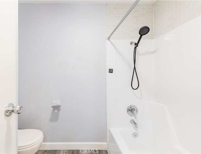 bathroom featuring toilet, baseboards, bathing tub / shower combination, and wood finished floors