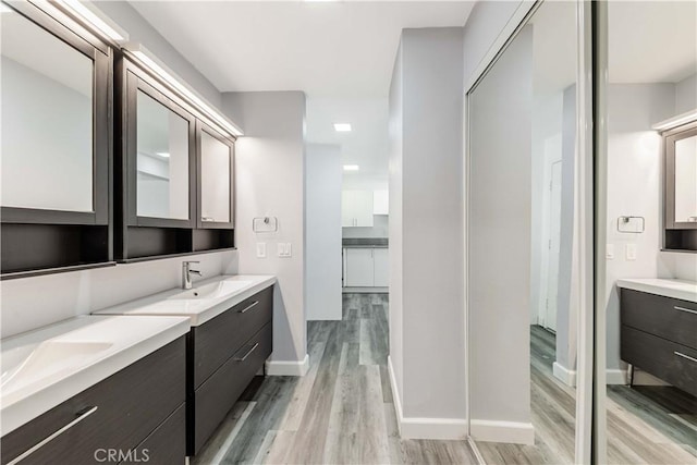 bathroom featuring a sink, two vanities, baseboards, and wood finished floors