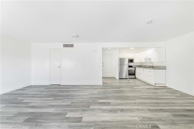 unfurnished living room with light wood finished floors, visible vents, baseboards, and a sink