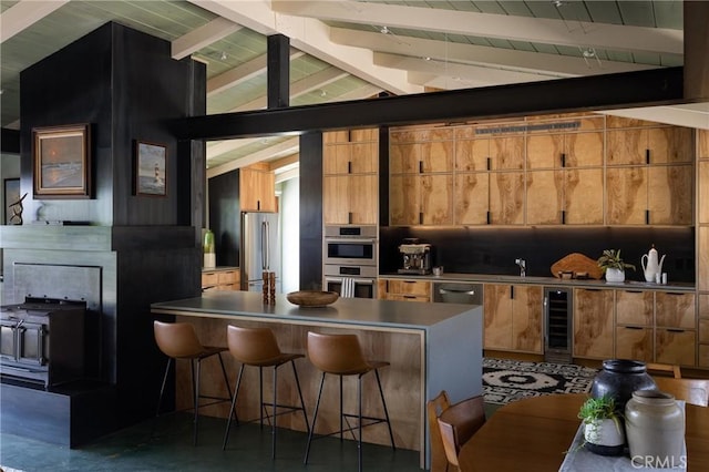 kitchen with lofted ceiling with beams, finished concrete floors, a kitchen bar, beverage cooler, and appliances with stainless steel finishes