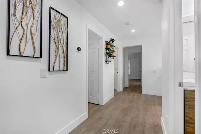 corridor with light wood finished floors, baseboards, and recessed lighting