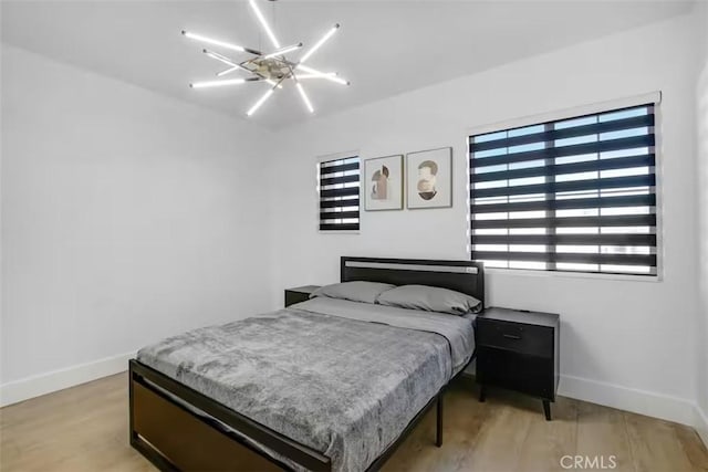 bedroom featuring light wood-type flooring, baseboards, and ceiling fan with notable chandelier