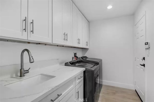 laundry room with washer and dryer, a sink, cabinet space, light wood-type flooring, and baseboards