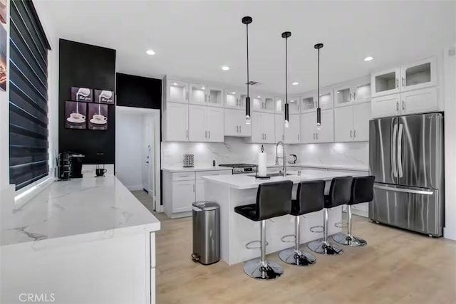 kitchen featuring glass insert cabinets, a sink, freestanding refrigerator, white cabinetry, and decorative backsplash