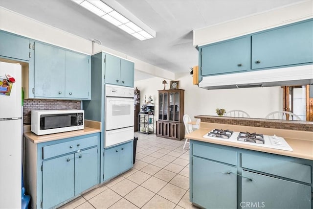 kitchen with light tile patterned floors, white appliances, blue cabinetry, a warming drawer, and light countertops