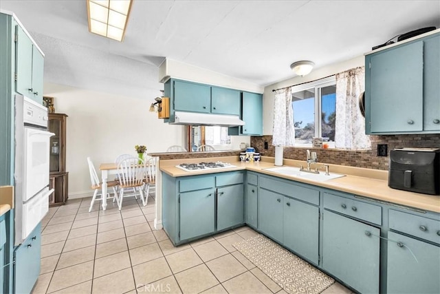 kitchen with white appliances, a sink, a warming drawer, light countertops, and light tile patterned flooring