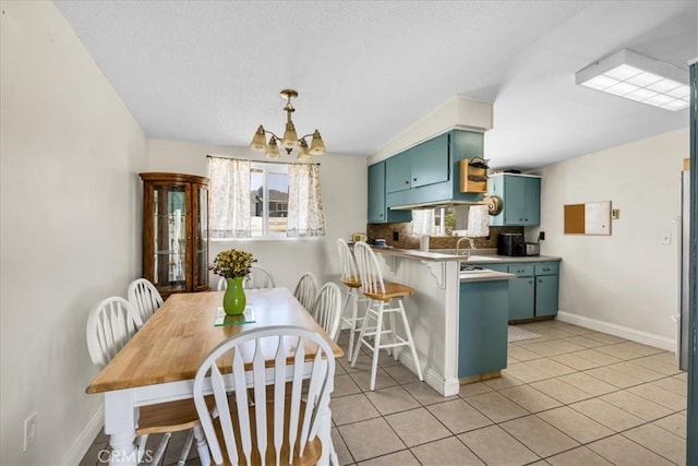 kitchen with a peninsula, green cabinetry, light tile patterned flooring, baseboards, and a notable chandelier