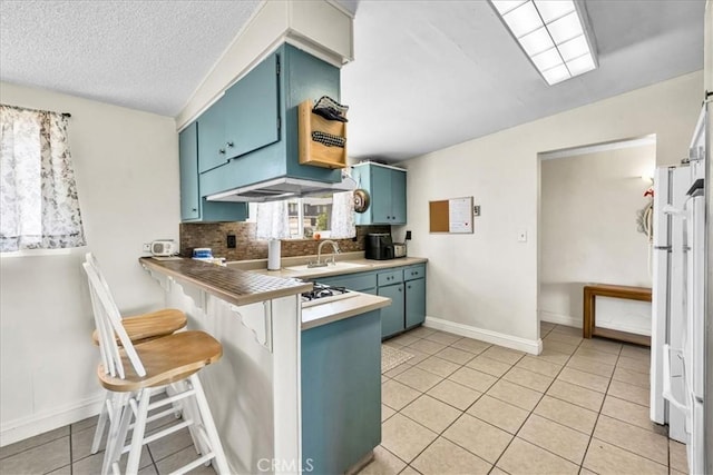 kitchen featuring a peninsula, light tile patterned floors, a sink, tasteful backsplash, and blue cabinets