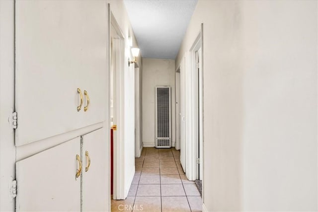 corridor featuring baseboards, light tile patterned floors, and a heating unit