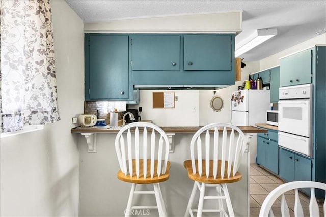 kitchen with light tile patterned floors, white appliances, a peninsula, a kitchen breakfast bar, and a warming drawer